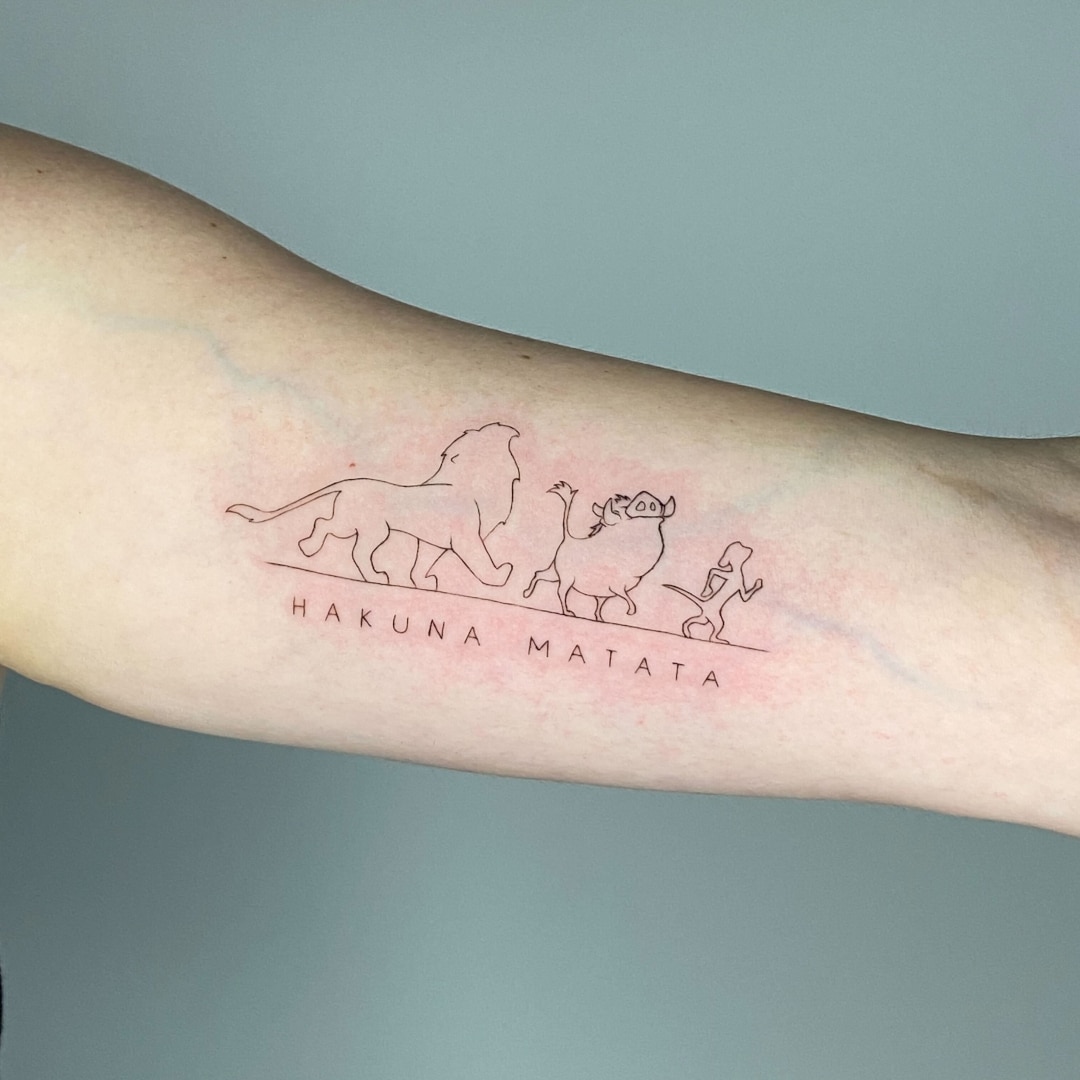 Tattoo depicting a lion, warthog, and meerkat with 'Hakuna Matata' text.