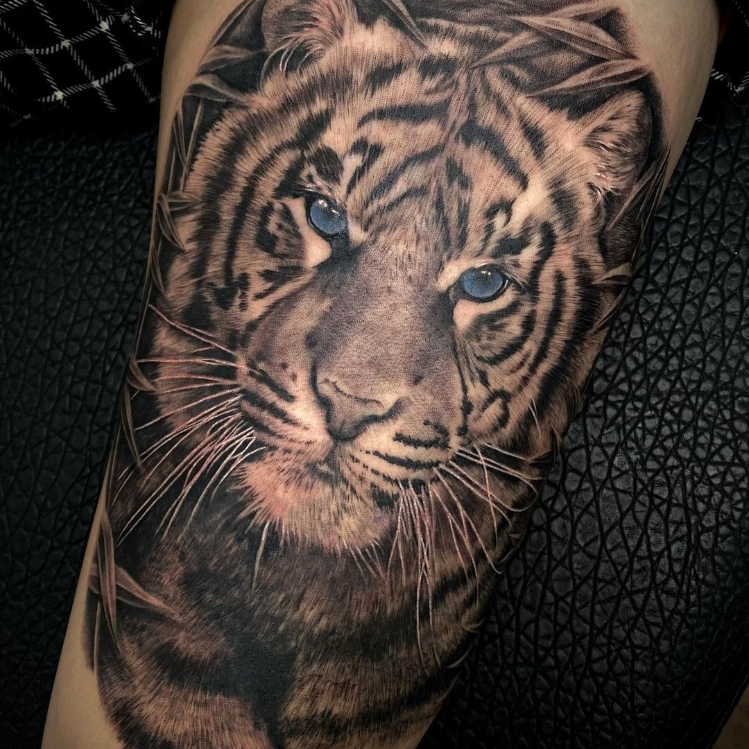 Realistic tattoo of a tiger's face with blue eyes.