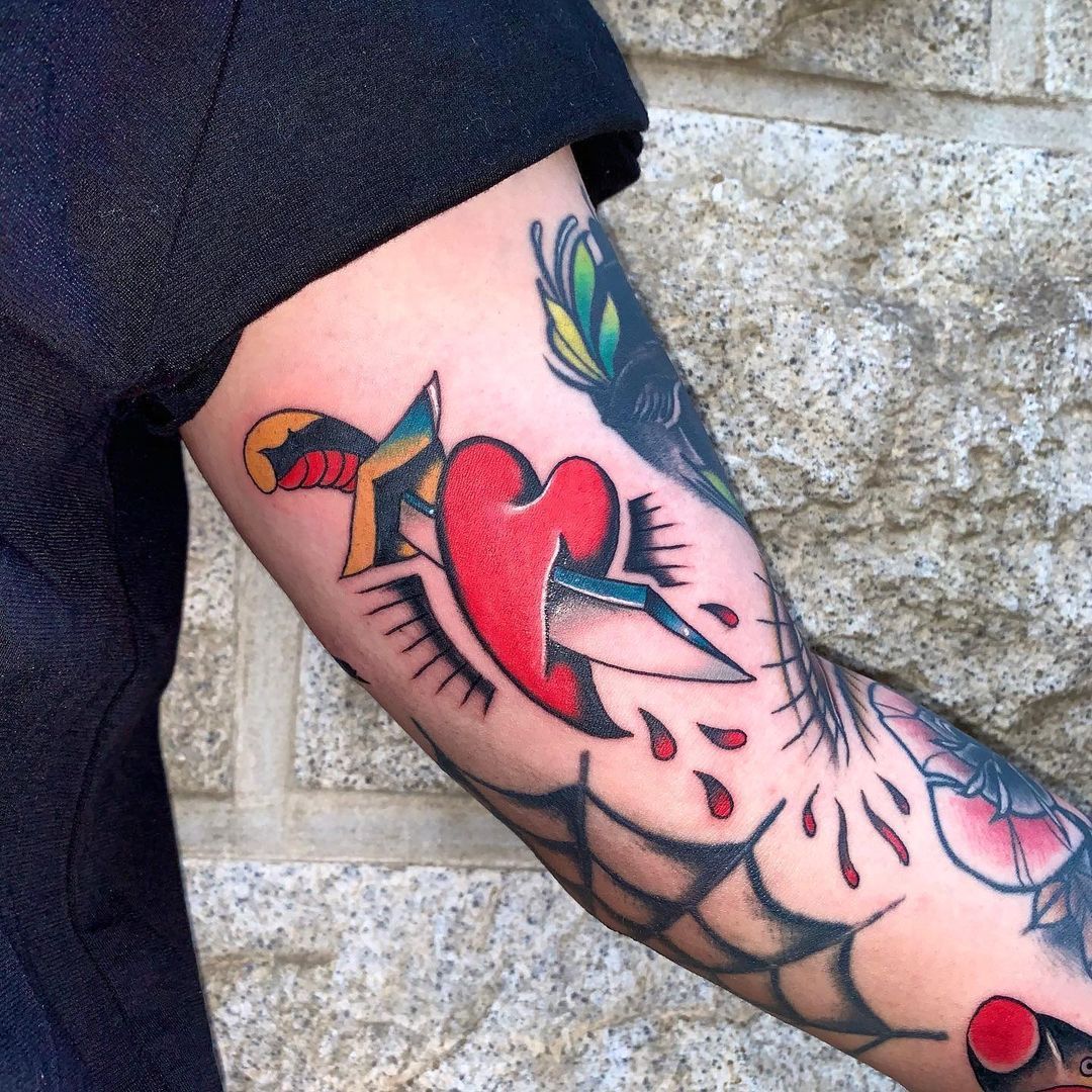 Colorful tattoo of a heart with a dagger on a forearm
