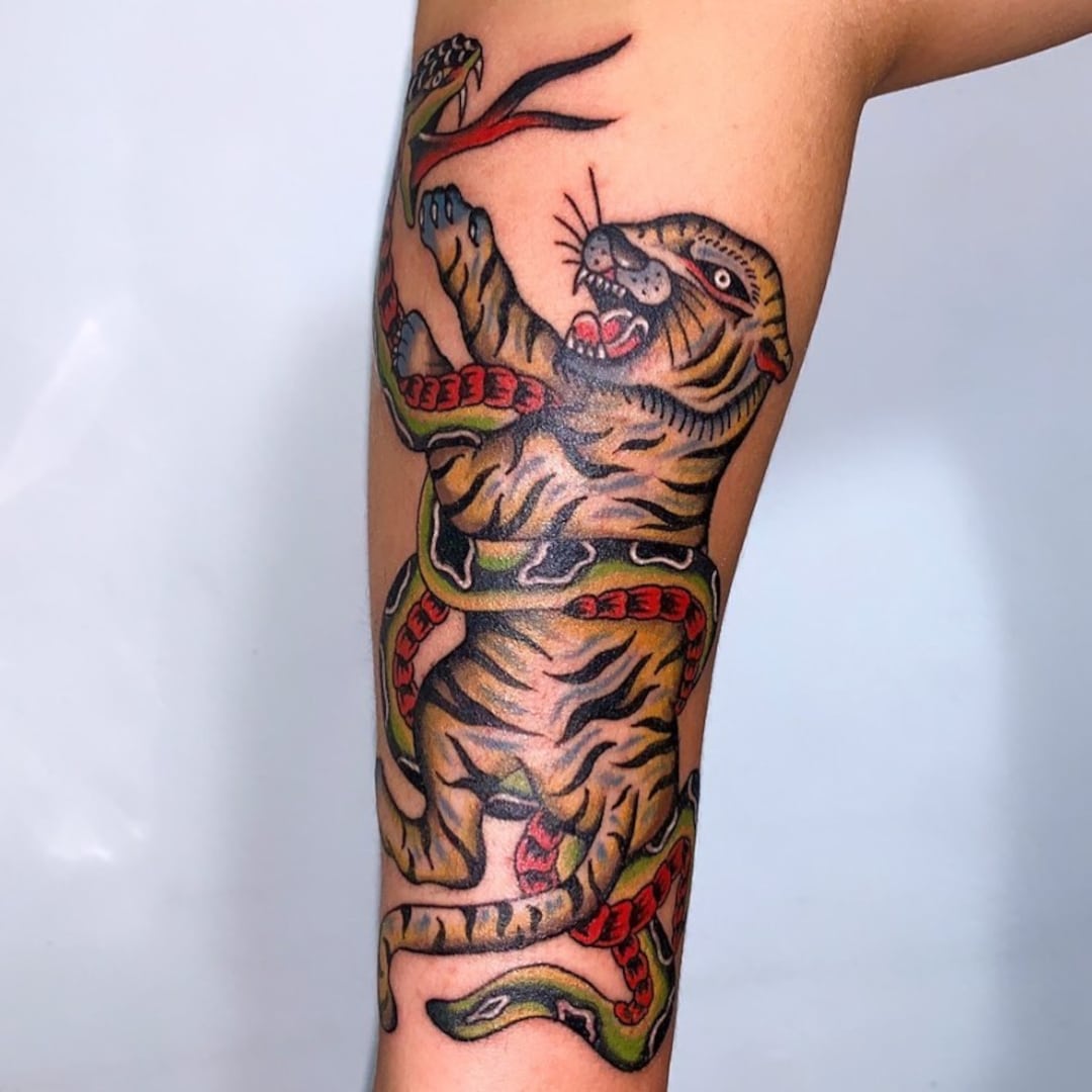 Tattoo of a tiger entwined with a snake on a forearm
