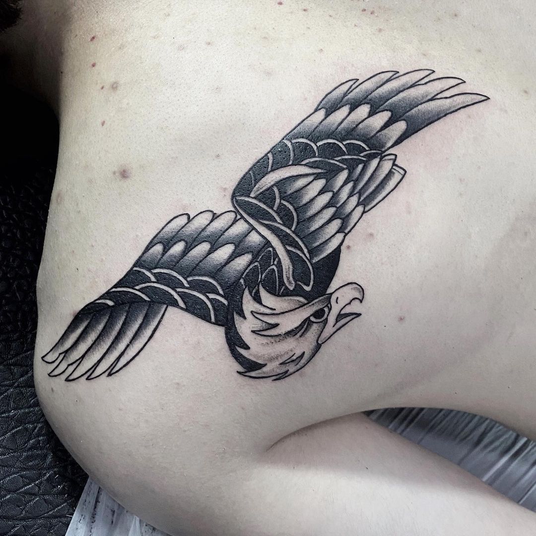 A detailed black and grey tattoo of an eagle in flight on skin.