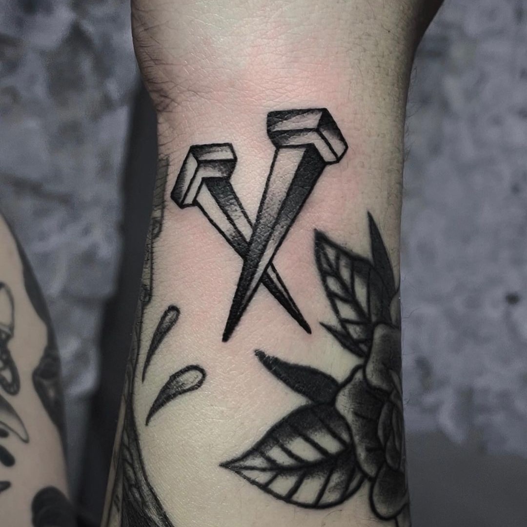 Black ink tattoo of two nails crossing on a forearm