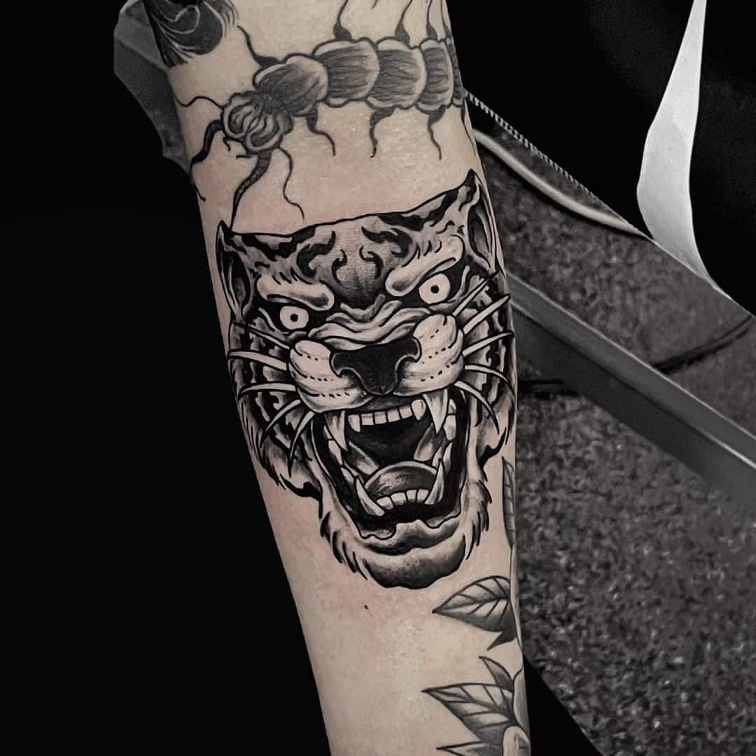Black and grey tattoo of a roaring tiger on forearm