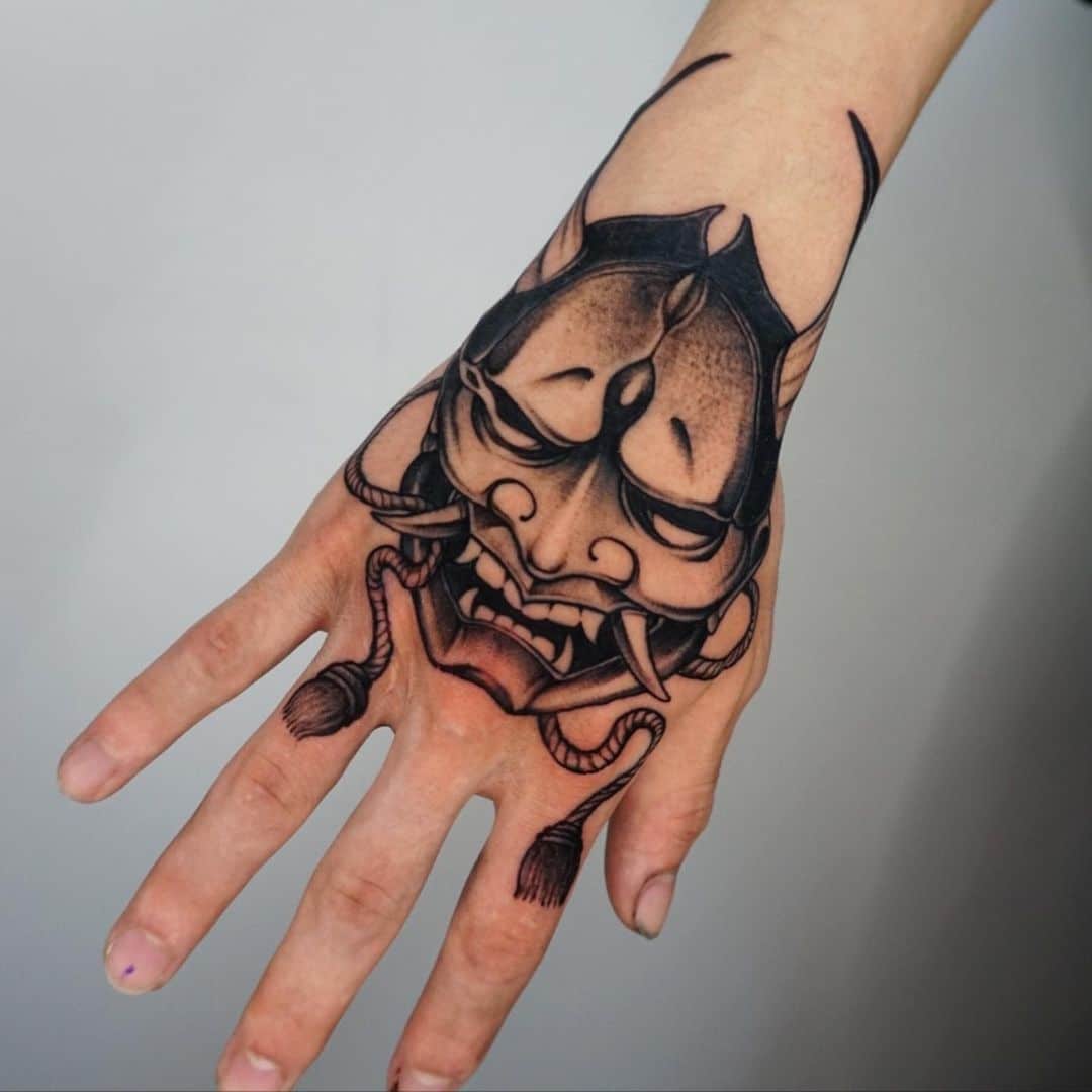 Hand tattoo featuring traditional mask design