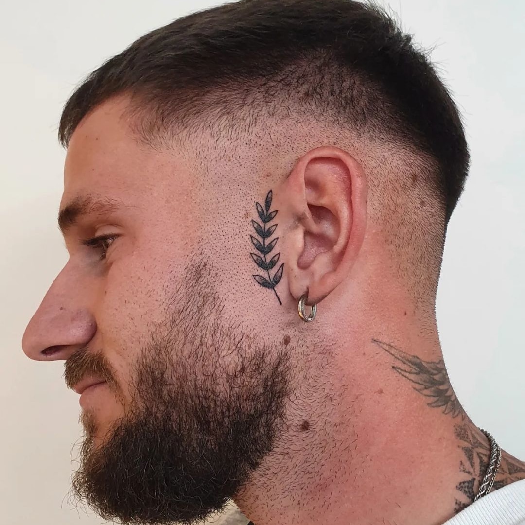 Profile view of a man with a leaf tattoo behind his ear