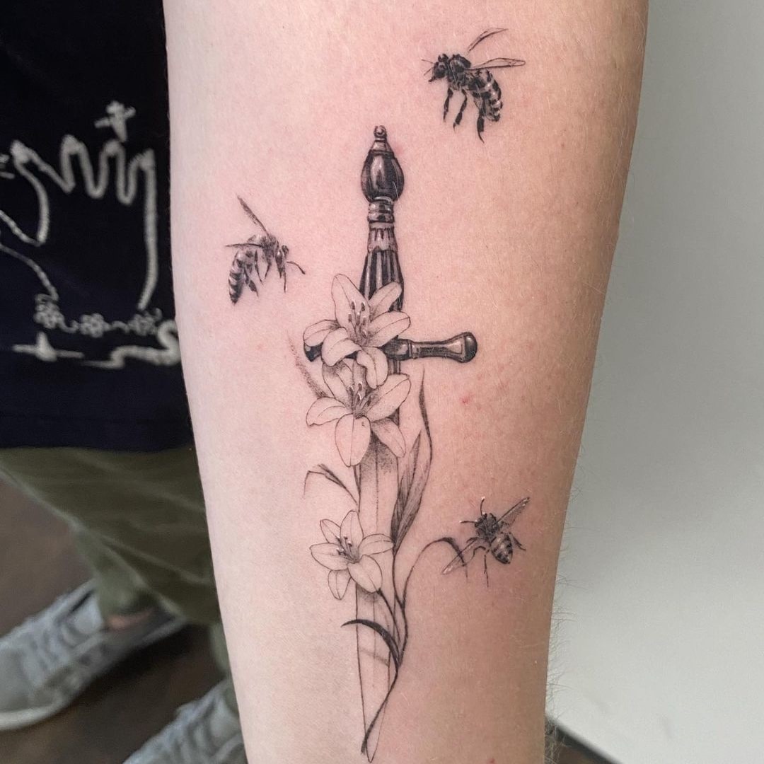 Tattoo of a sword, bees, and flowers on an arm